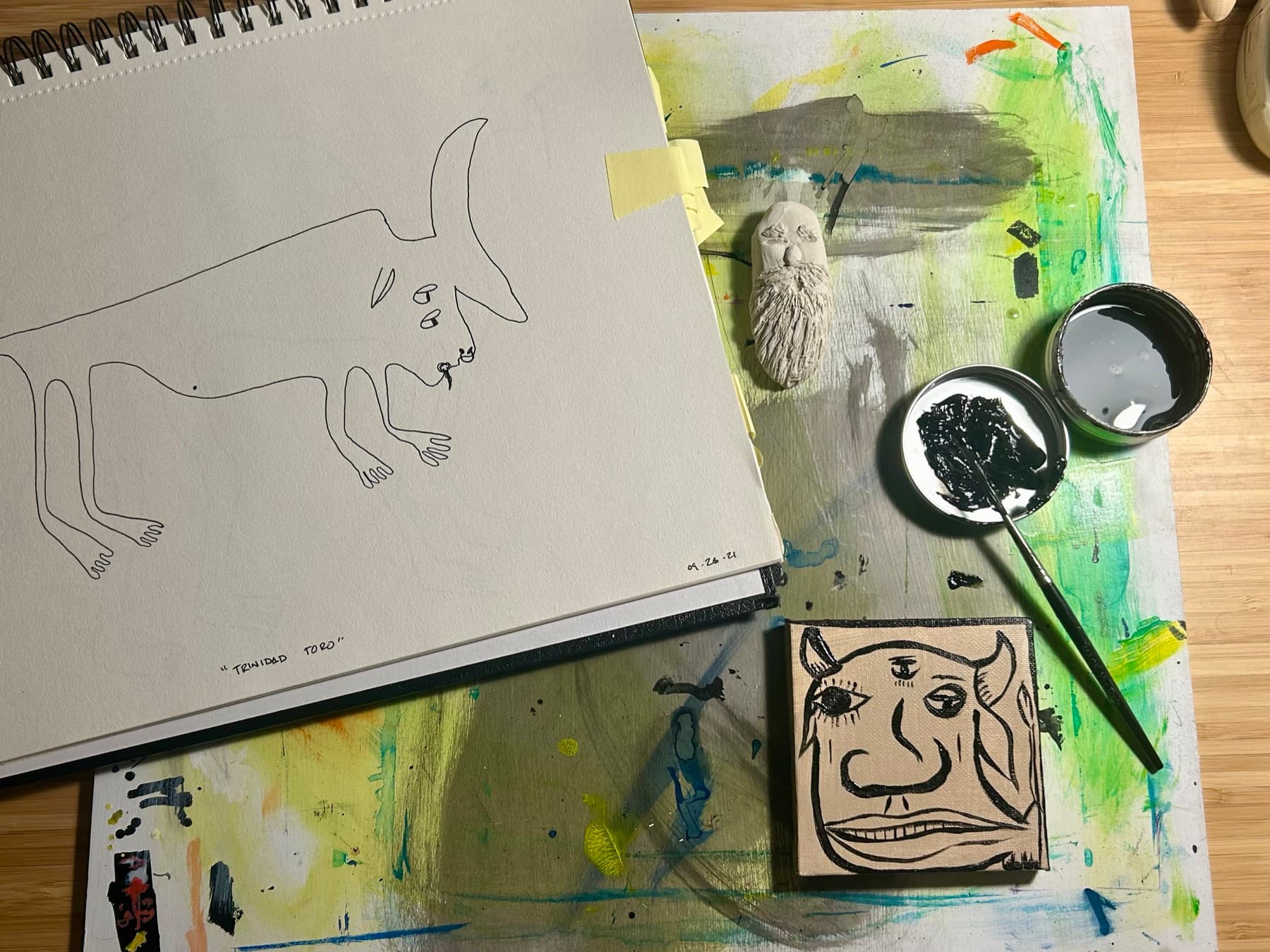 A sketchbook creature drawn in ink beside ink pots on a paint-covered work surface